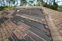 A roof with a lot of shingles missing and trees in the background