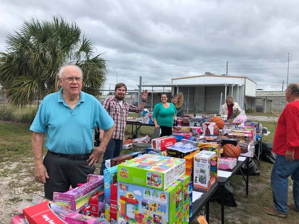 A group of people are standing around a table filled with lots of toys.