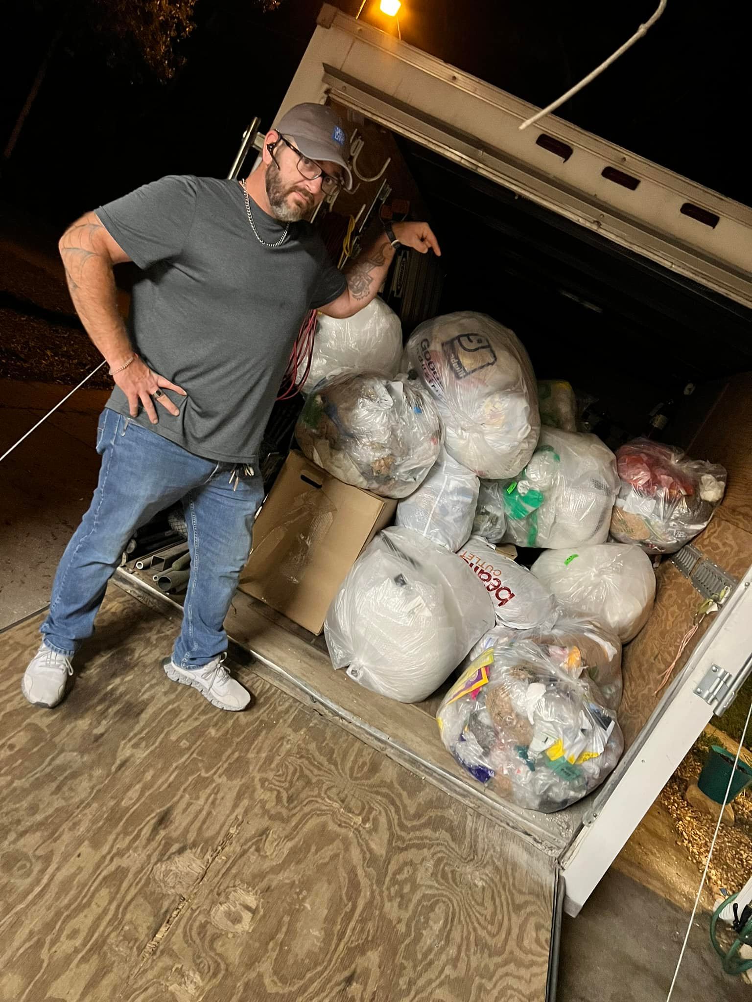A man is standing in front of a truck filled with bags of trash.