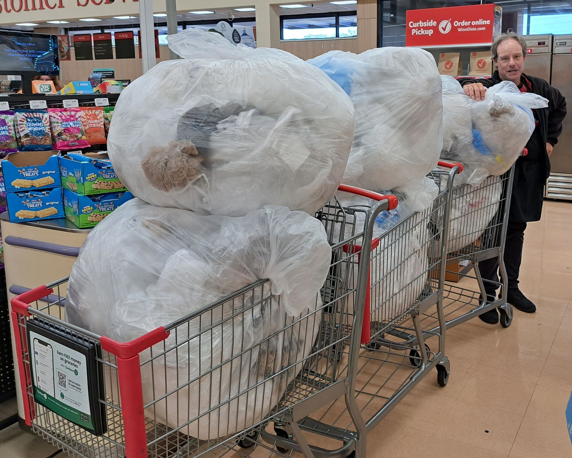 A man is standing next to a shopping cart filled with bags of toilet paper