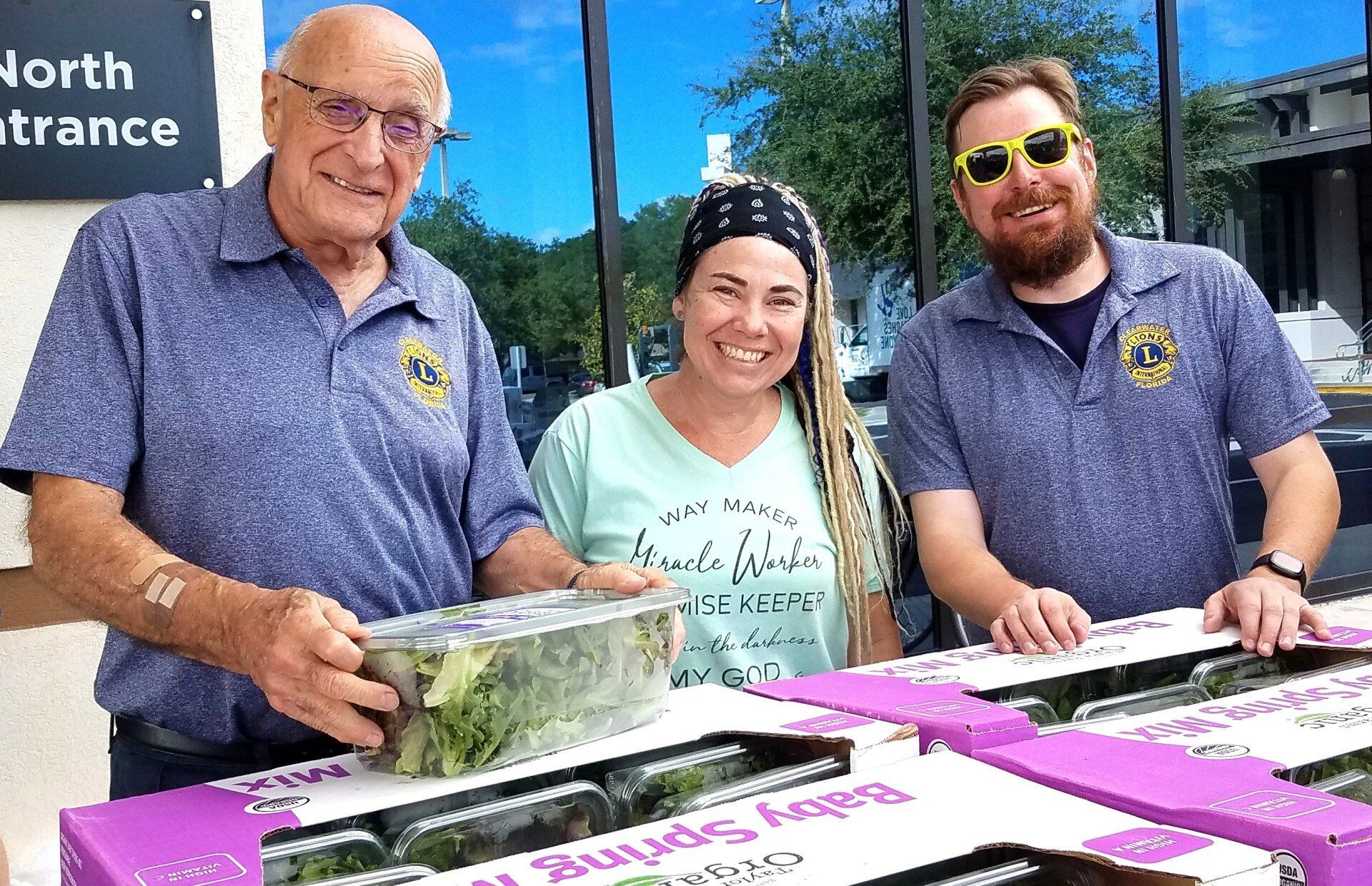 Three people are standing next to each other in front of boxes of food.