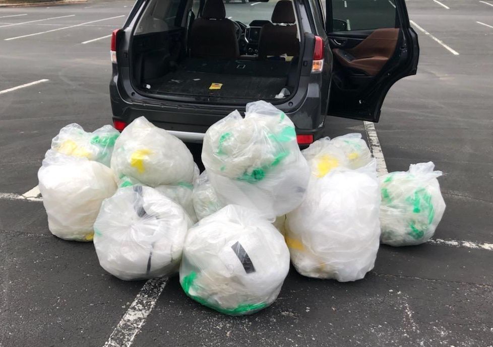 A pile of trash bags in front of a car in a parking lot.