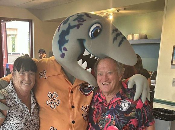 A man and woman are posing for a picture with a shark mascot.