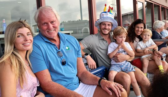 A group of people are sitting next to each other and one of them is wearing a birthday hat.
