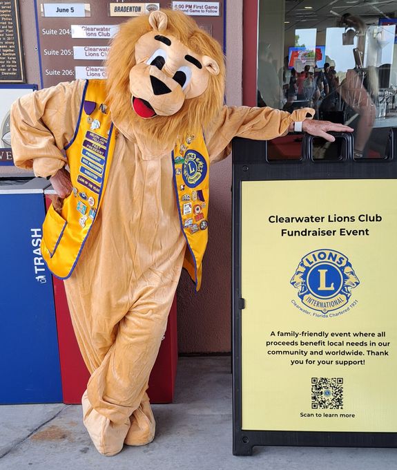 A lion mascot is standing next to a sign that says lions club