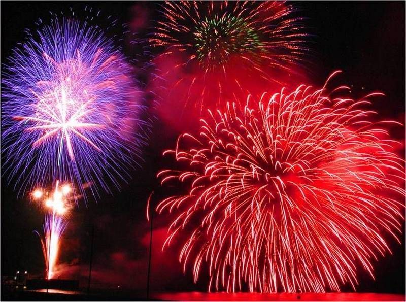 Fuochi d'artificio che esplodono in rosso, viola e verde contro un cielo notturno buio.