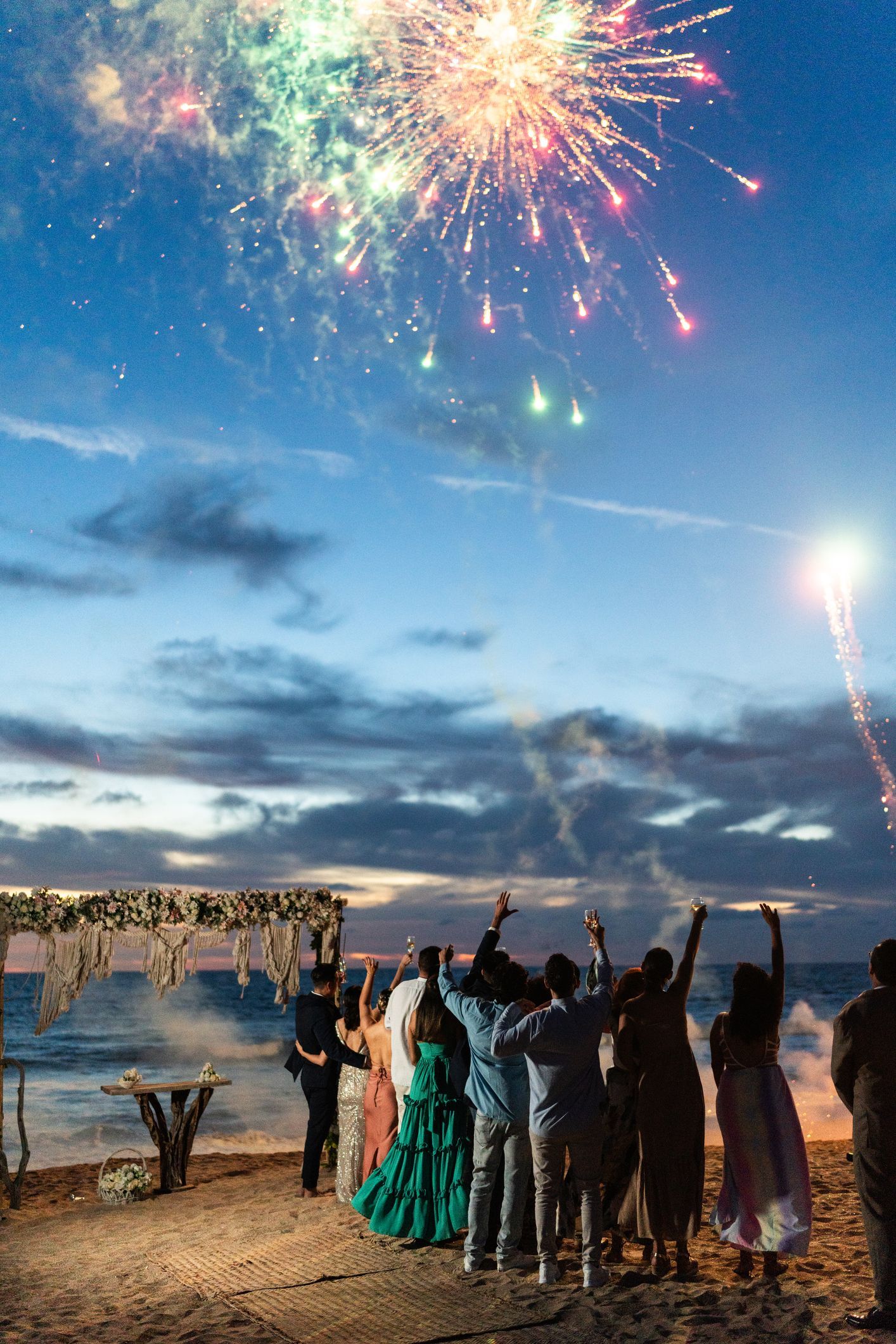 La gente sulla spiaggia guarda i fuochi d'artificio esplodere sull'oceano.