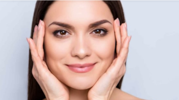 A woman is touching her face with her hands and smiling.