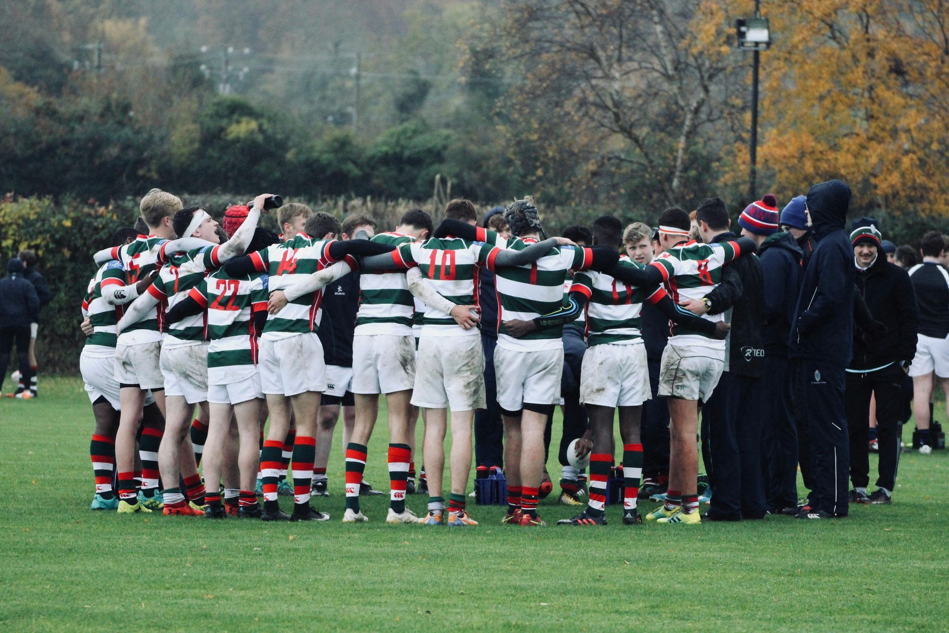 On voit une équipe de jeunes joueurs de rugby qui forme un cercle, les bras dessus et dessous et ils se parlent.