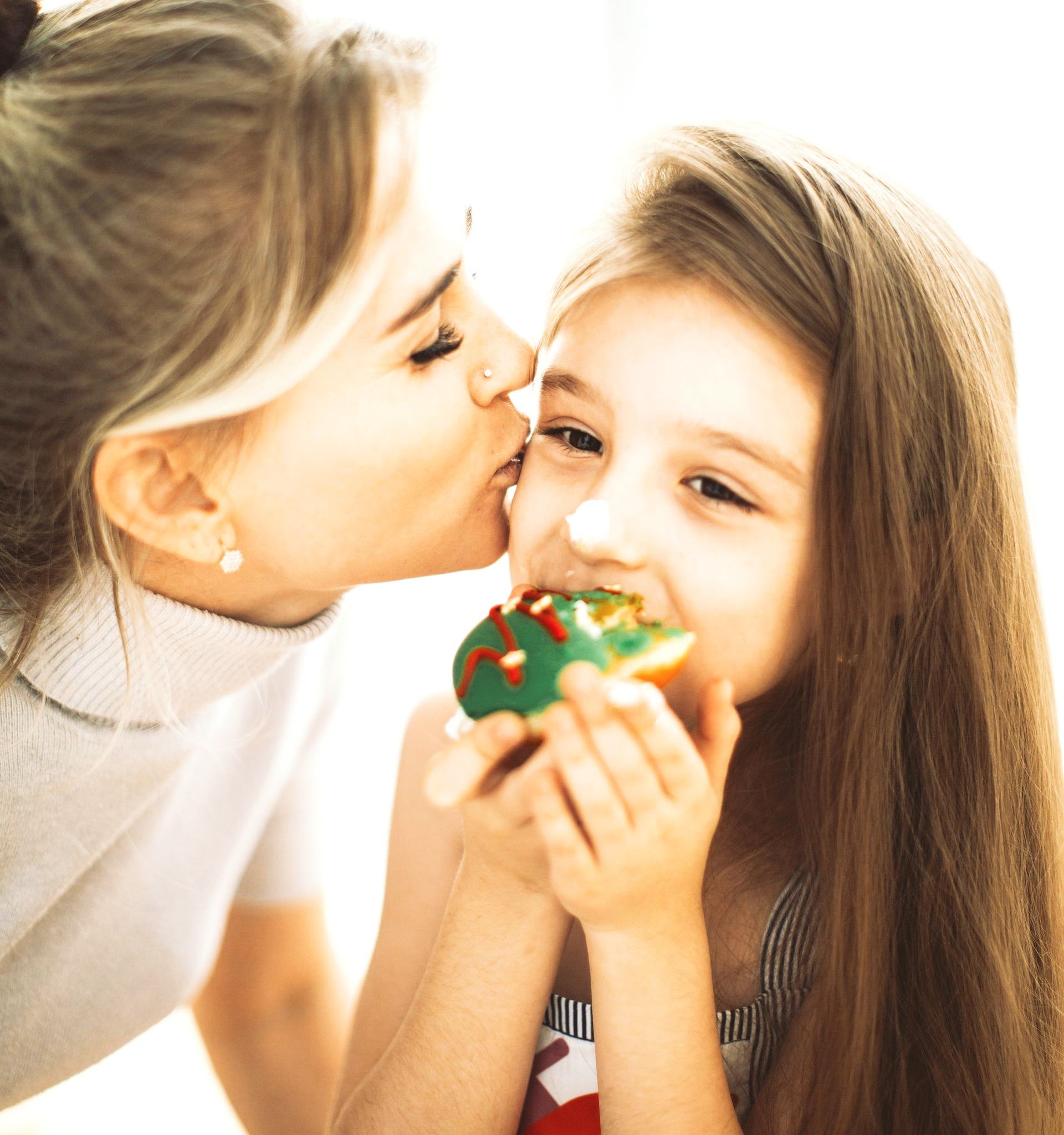 Bedingungslose Liebe ist der Schlüssel Eine elegant gekleidete Mutter küsst ihre 6jährige Tochter auf die Wange. Das Mädchen isst gerade ein Törtchen und hat die Nase mit Zucker verschmiert. Man kann die Liebe zwischen den beiden spüren.