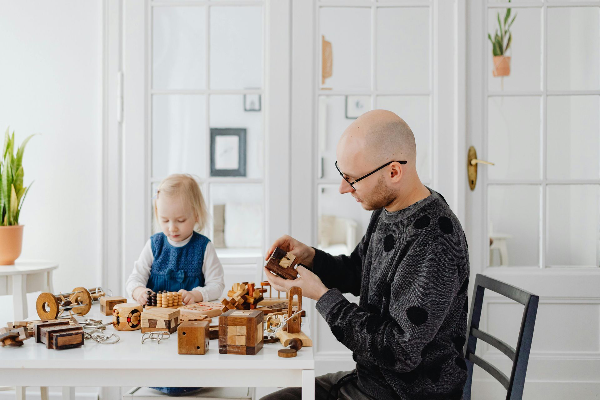 Vater Kind Zeit Ein Vater spielt mit seiner 4jährigen Tochter am Esstisch. Darauf befinden sich sehr viele Holzspielzeuge und Logikspiele. Der Raum ist freundlich hell und nüchtern.