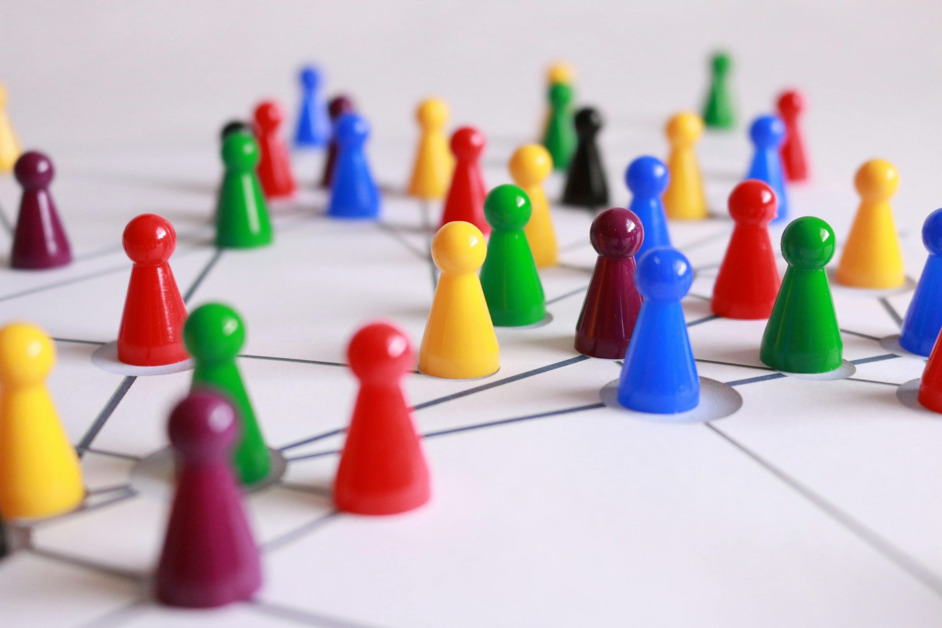 Auf dem Bild sind viele Spielfiguren in unterschiedlichen Farben zu sehen. Sie befinden sich auf einem Spielfeld, das einzelne Figuren miteinander verbindet als Andeutung der menschlichen Verbindungen in der Berufswelt.