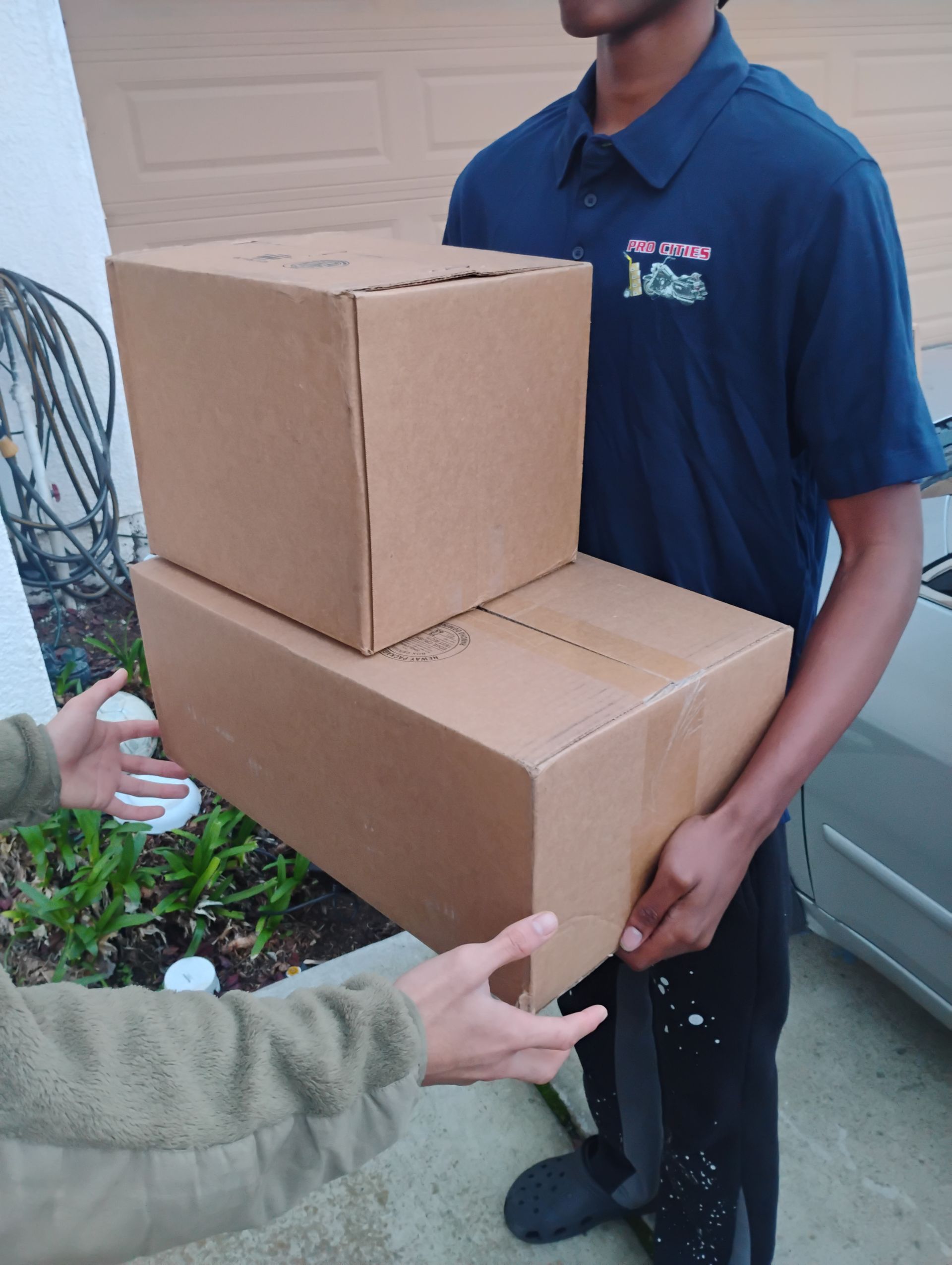 A man in a blue shirt is carrying two cardboard boxes