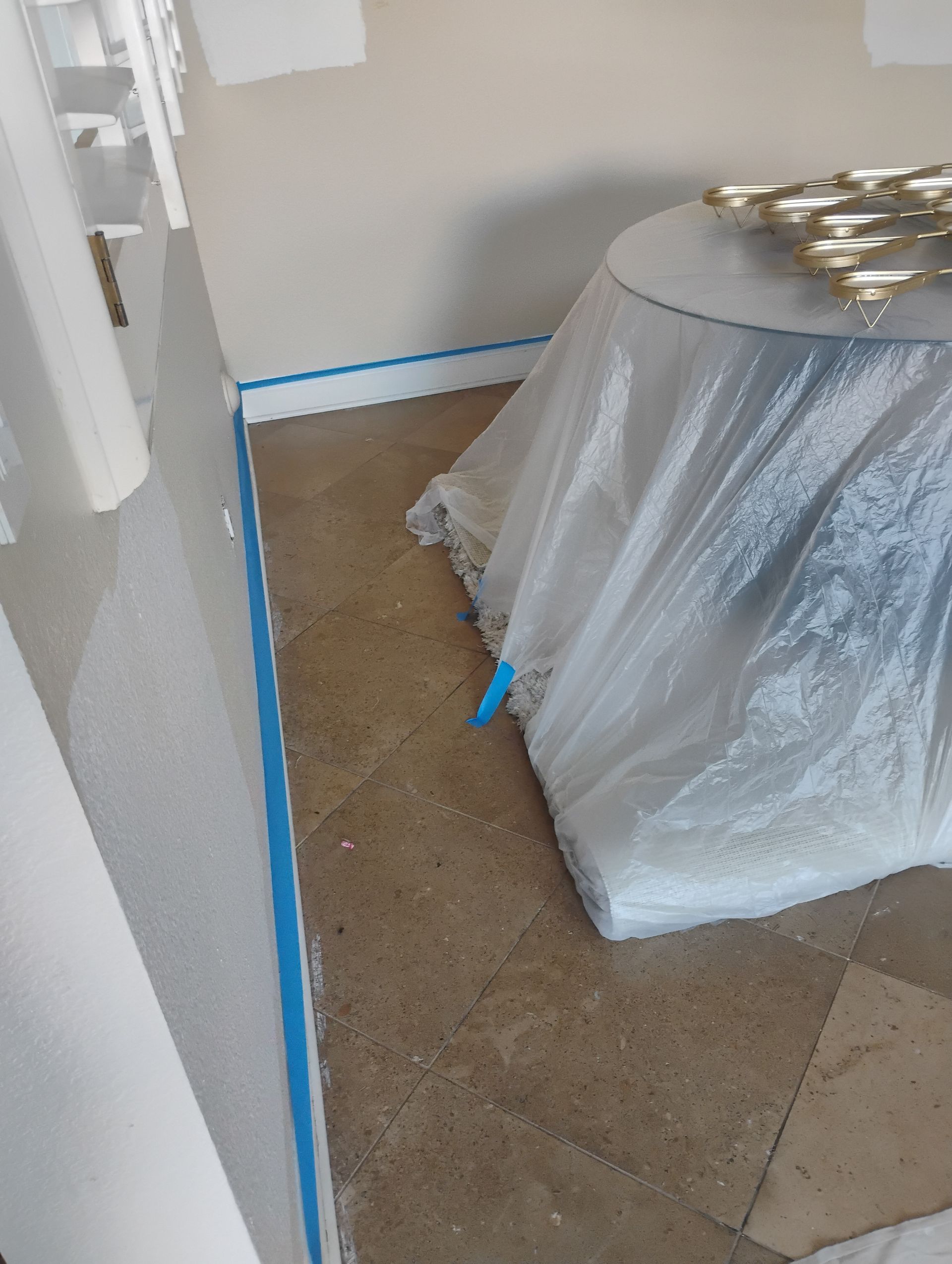 A table is covered in plastic while being painted in a room.