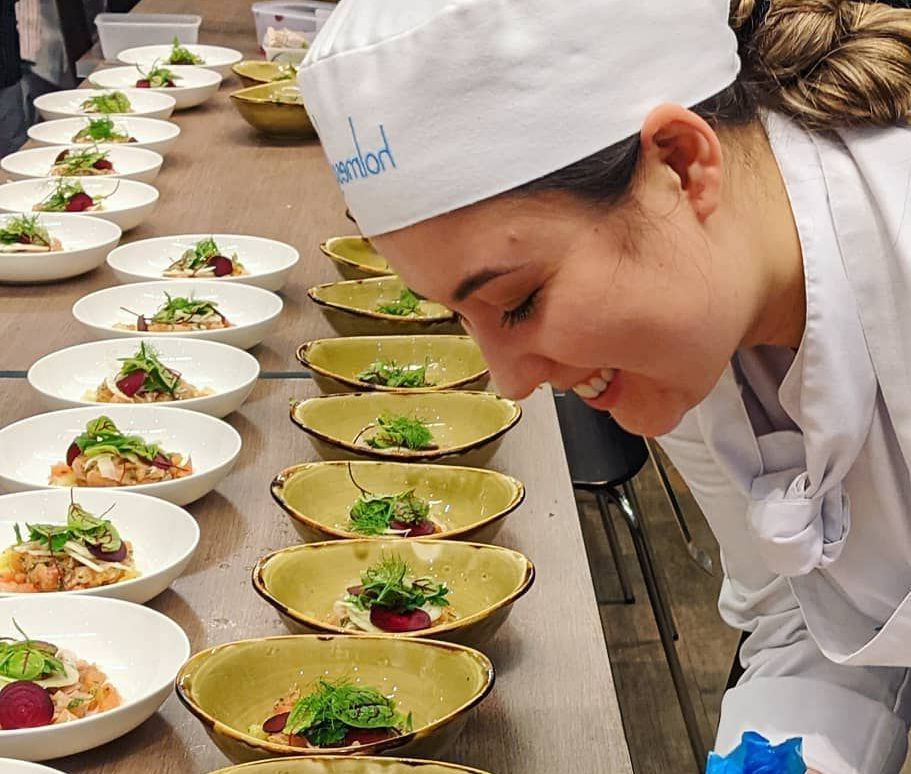 A woman in a chef 's hat is looking at bowls of food on a table.