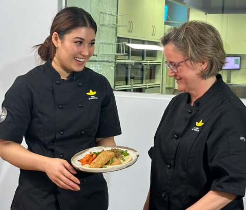 Two women are standing next to each other and one is holding a plate of food