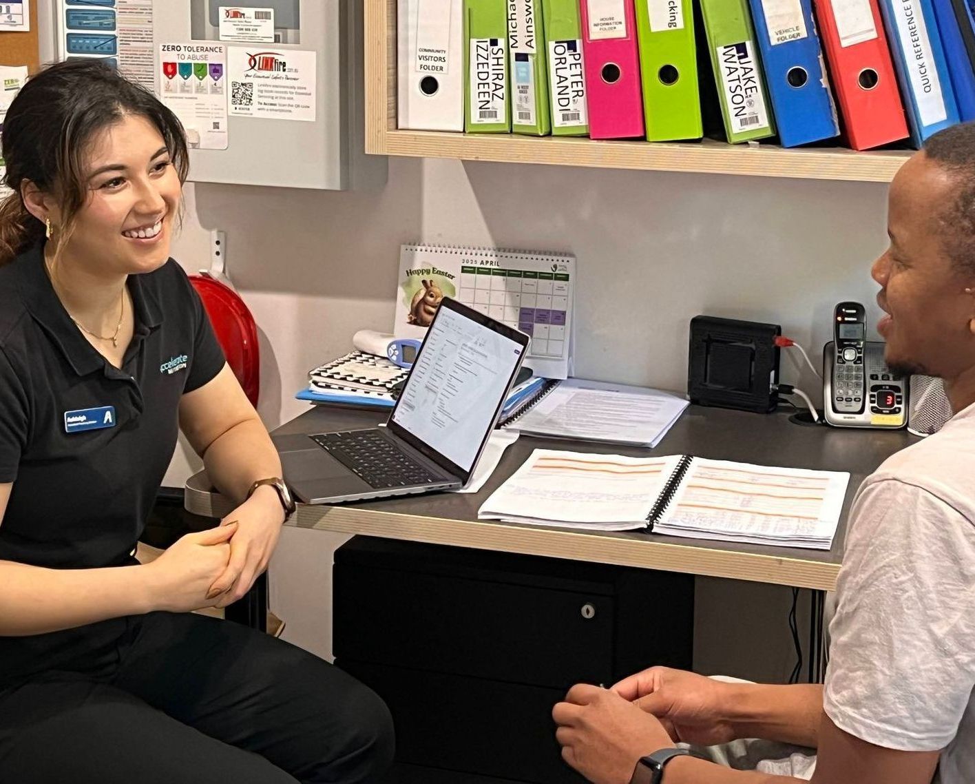 A man and a woman are sitting at a desk talking to each other.