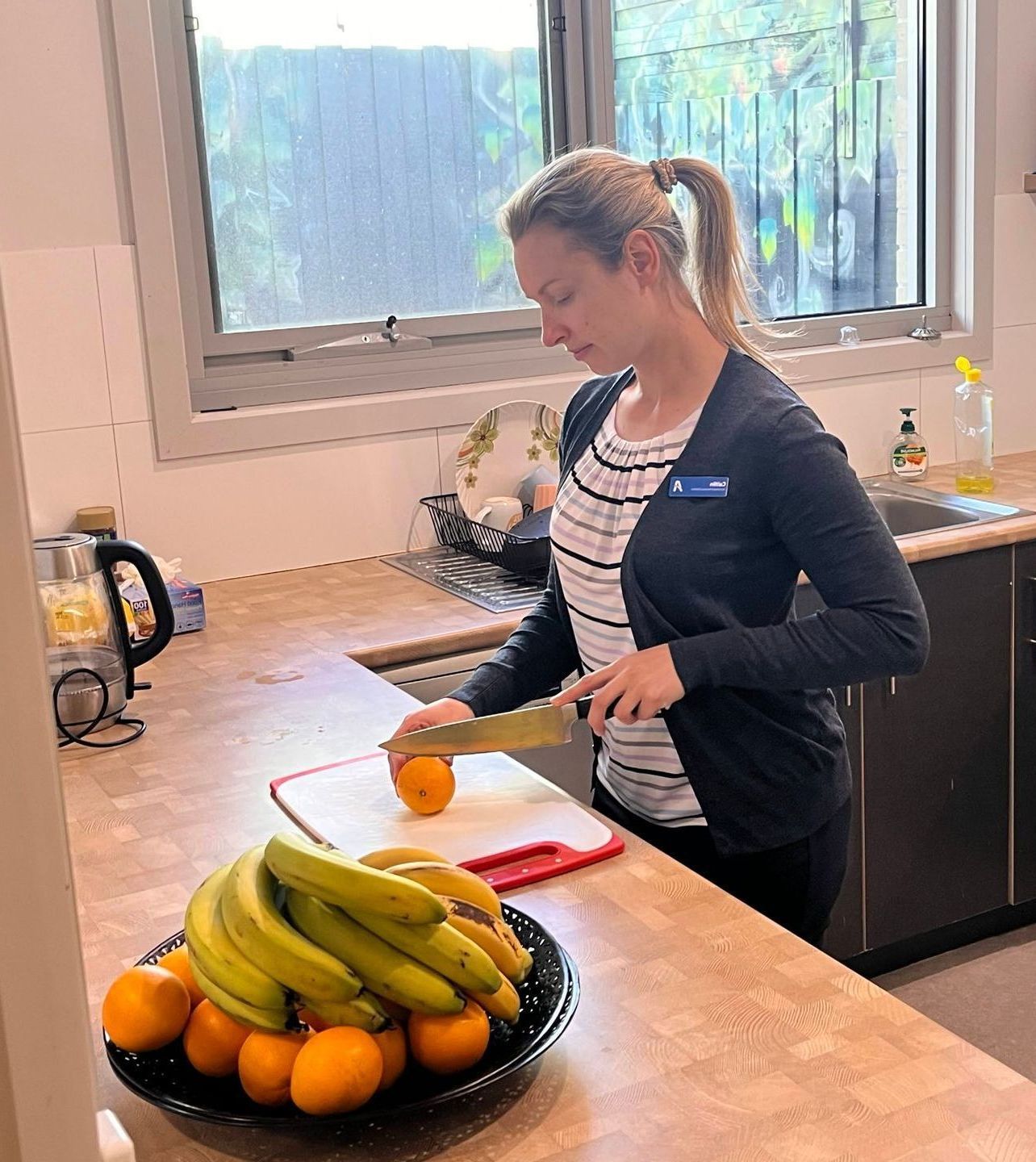 A woman is cutting an orange on a cutting board in a kitchen.