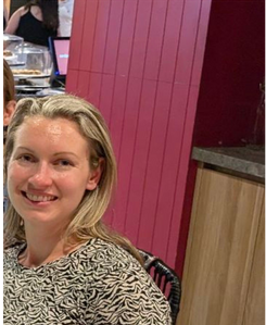 A woman is smiling while sitting at a table in front of a pink wall.