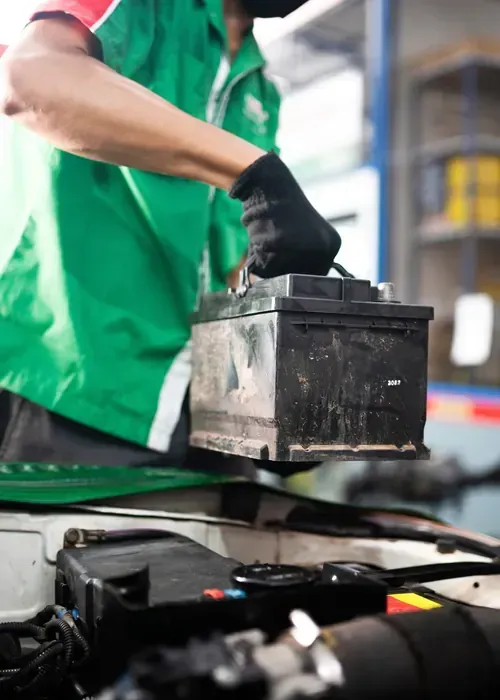 A person holding a red and black digital multimeter to test an engine under the hood of a car.