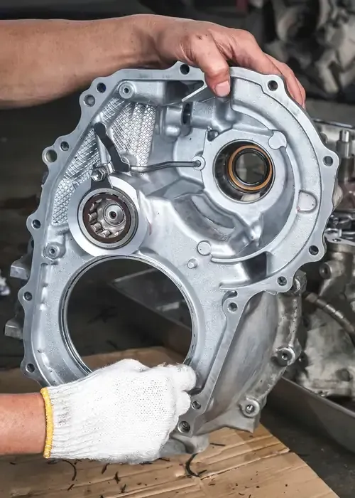 A person holding a red and black digital multimeter to test an engine under the hood of a car.