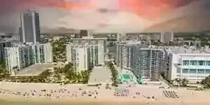 Aerial view of a beach lined with high-rise buildings under a colorful sunset sky