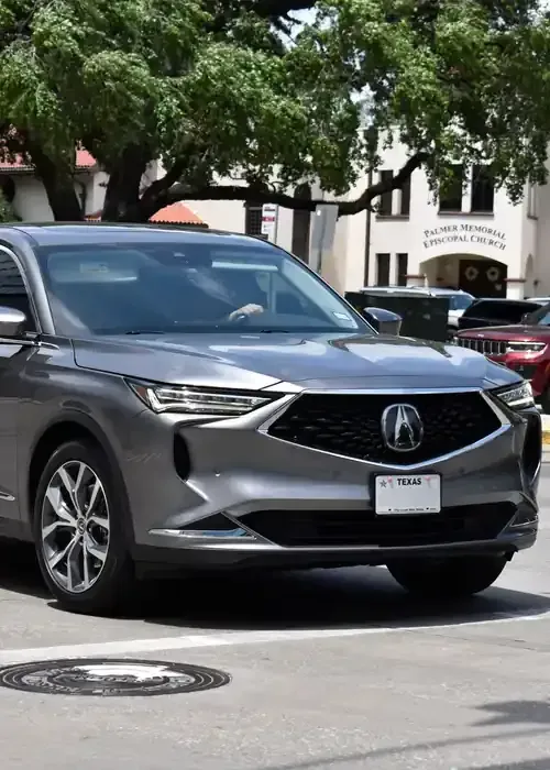 A gray Acura SUV waiting at a street intersection, with a church building visible in the background.