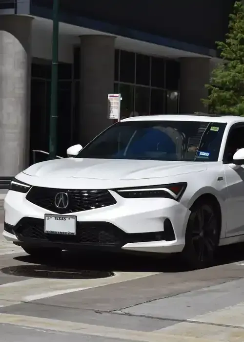 A white Acura Integra sedan sits parked on a city street in front of a modern building.