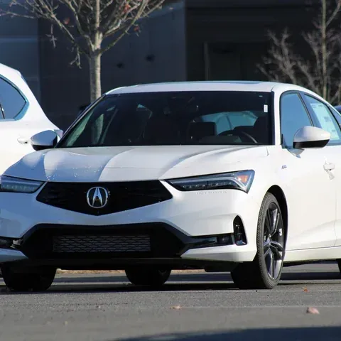 A white Acura Integra sedan parked in a sunny outdoor lot with trees in the background.