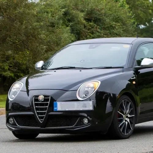 A black Alfa Romeo MiTo hatchback driving on an asphalt road with trees in the background.