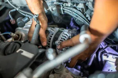 A mechanic's hands work on an alternator installed inside a vehicle's engine bay.