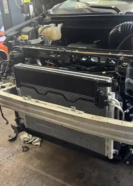A mechanic's hands work on an alternator installed inside a vehicle's engine bay.