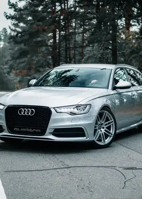 A silver Audi station wagon parked on an asphalt road in front of a forest.