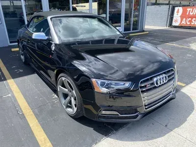 A black Audi convertible parked in a dealership lot on a sunny day.