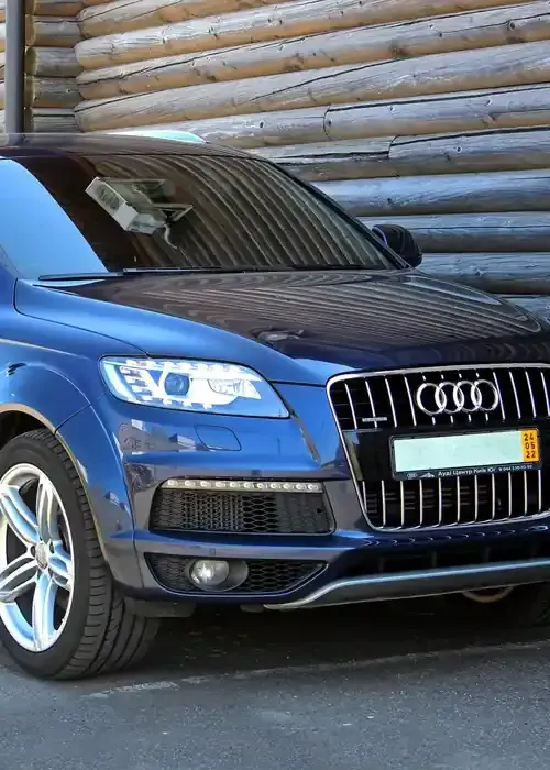 A dark blue Audi Q7 SUV parked in front of a horizontal log wall.