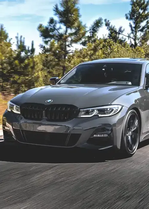 A grey BMW sedan driving on a road surrounded by trees.