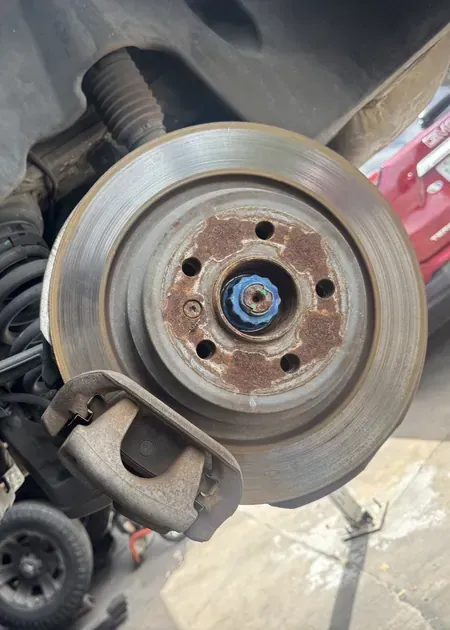 A person holding a red and black digital multimeter to test an engine under the hood of a car.