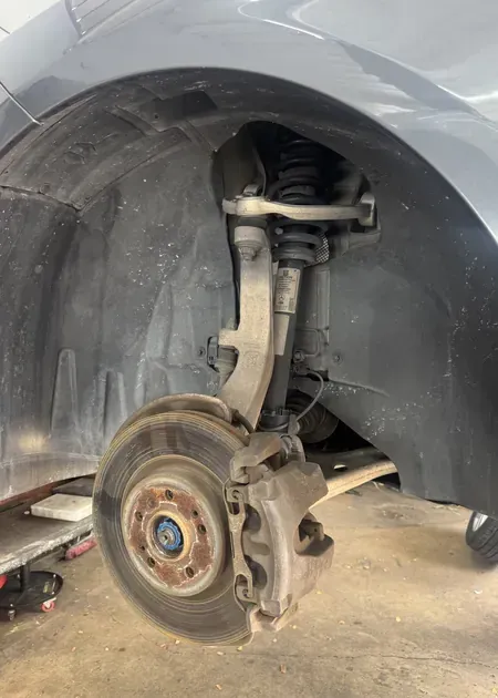 A person holding a red and black digital multimeter to test an engine under the hood of a car.