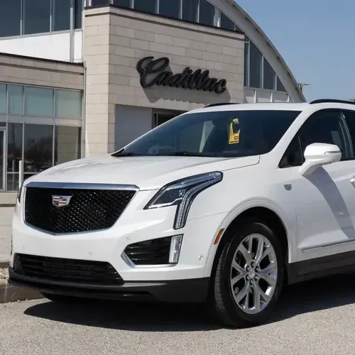 A white Cadillac XT5 SUV parked in front of a Cadillac dealership building.