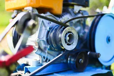 A mechanic's hands work on an alternator installed inside a vehicle's engine bay.