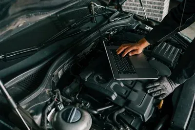 A mechanic's hands work on an alternator installed inside a vehicle's engine bay.