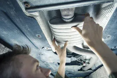 A mechanic's hands work on an alternator installed inside a vehicle's engine bay.
