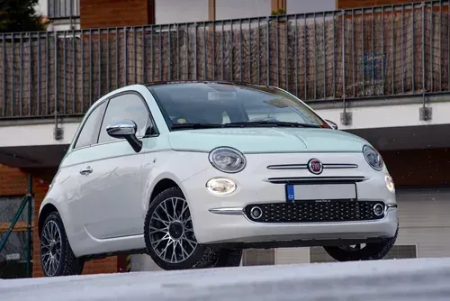 A white and light green two-tone Fiat 500 hatchback parked on a paved surface in front of a building.