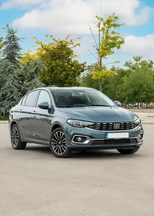 A grey Fiat Tipo sedan parked on an asphalt lot with trees and a blue sky in the background.
