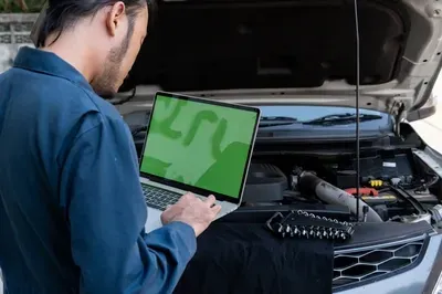 A mechanic's hands work on an alternator installed inside a vehicle's engine bay.