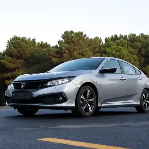 A silver Honda Civic sedan parked on an asphalt road in front of trees.