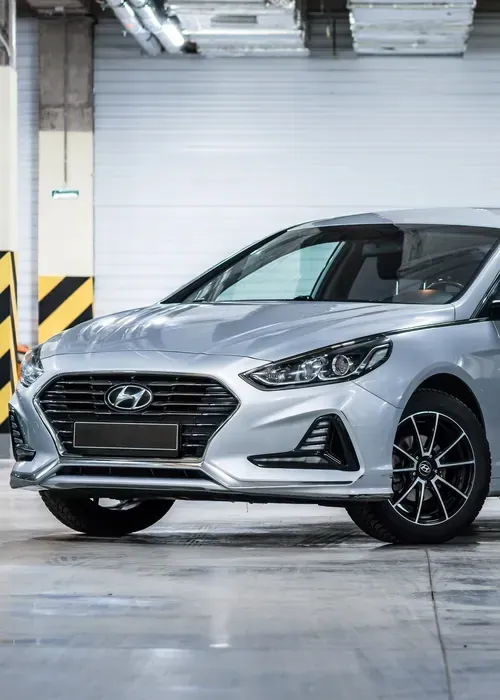 A silver Hyundai sedan parked indoors on a concrete floor in front of a white wall.