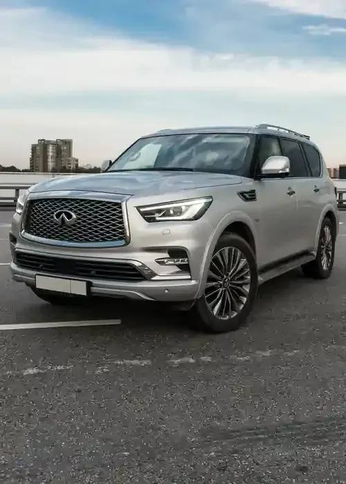 Silver Infiniti QX80 luxury SUV parked on asphalt with a blurred city skyline in the background.