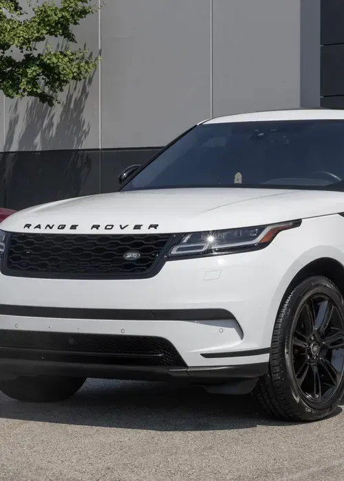 A white Land Rover Range Rover Velar parked outdoors against a grey wall with black wheels and grille.