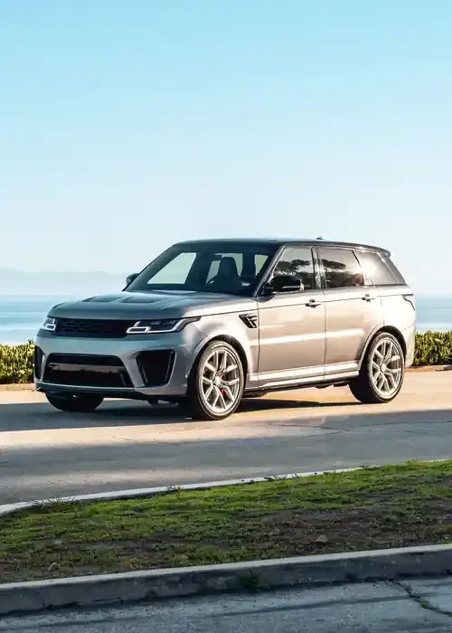 Silver Land Rover Range Rover parked on a coastal road overlooking the ocean under a clear blue sky.